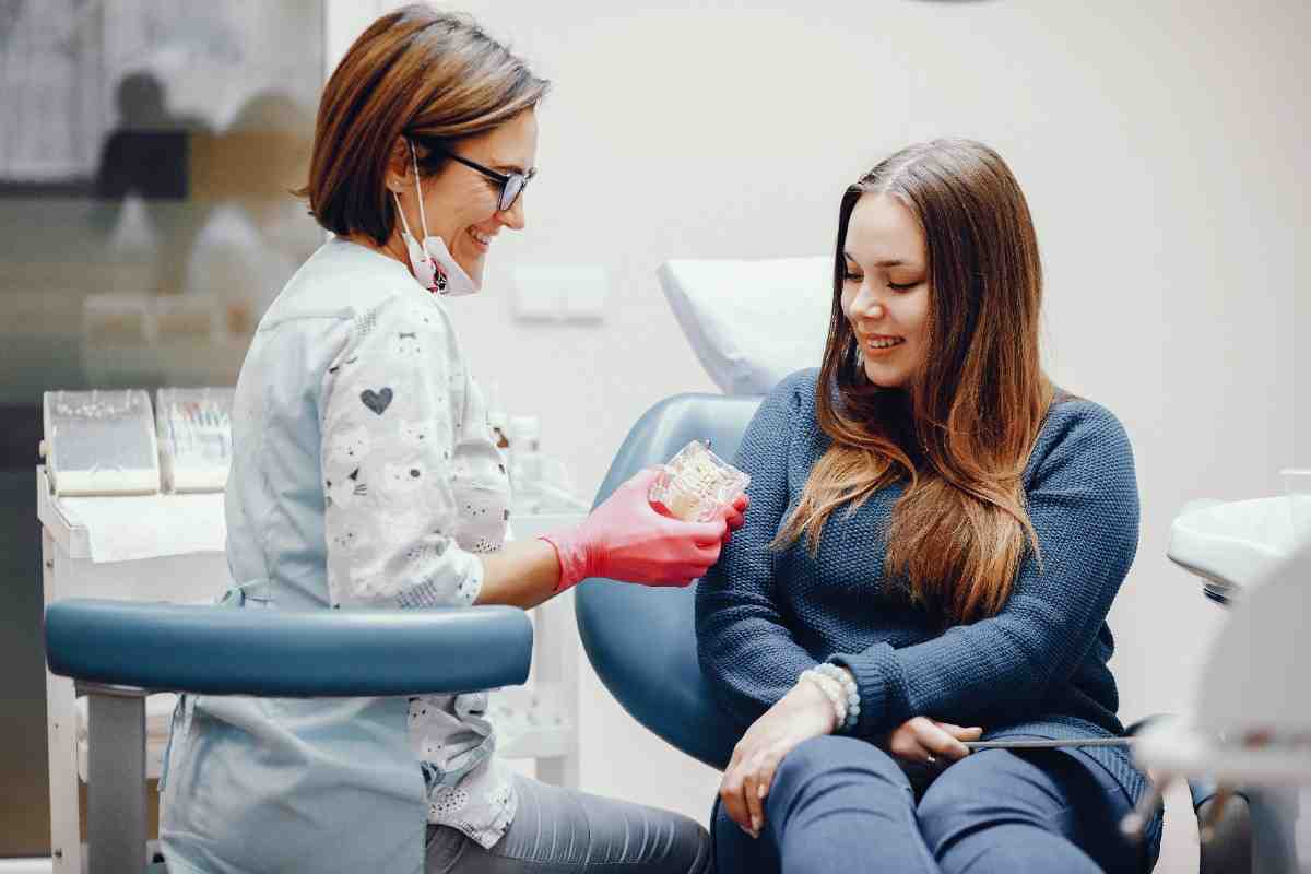 Dentist wearing red gloves showing a set of dentures to a smiling female patient seated in a dental chair during a consultation.