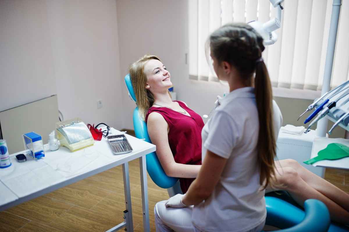 Dentist consulting with a female patient reclining in a dental chair, discussing treatment options in a modern dental exam room.